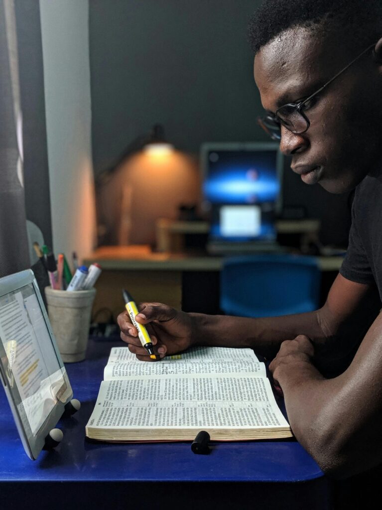 pexels-photo-2574616-2574616 Man deeply engaged in studying with a book and tablet at a desk